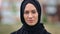 Closeup face of beautiful young Arabic woman in black hijab smiling posing outdoor at city building