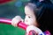 Closeup face of cute Asian girl using her mouth to touch object of playground equipment.