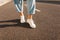 Closeup fashionable female legs in stylish blue pants in a white trendy sneakers stand on the asphalt on a bright sunny day.