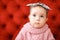 Closeup female child wearing pink sweater sitting in red background.