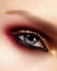 Closeup female eye with fashion bright make-up. Beautiful gold, red eyeshadow, glitter, black eyeliner. Shape Eyebrows