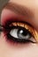 Closeup female eye with fashion bright make-up. Beautiful gold, red eyeshadow, glitter, black eyeliner. Shape Eyebrows