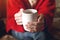 Closeup of female hands with a cup of beverage. Beautiful girl in red sweater holding cup of tea in the morning sunlight