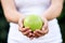 Closeup of female hands holding big shiniy green apple. Anonymous middle-aged woman giving or offering apples standing at farm.