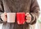 Closeup of female hands with a pink red mug coffee beverage. Beautiful girl in grey sweater holding cup of tea or coffee