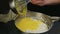 Closeup female hands pour whisked egg yolks into metal bowl with yeast dough