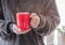 Closeup of female hands with a red mug coffee beverage. Beautiful girl in grey sweater holding cup of tea or coffee in the morning