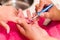 Closeup females hands getting manicure treatment from woman using small brush in salon environment, pink towel surface