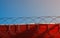 Closeup of a fence with barb wire curving in loops on a red building against the blue sky