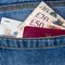 Closeup of fifty, twenty, ten pounds sterling banknotes, contactless credit card and EU passport peeking out of blue jeans back