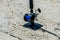 Closeup of a fishing rod with blue reel resting on a rod hole on a concrete surface