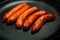 Closeup five short fried hunting sausages on round black pan