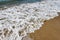 Closeup of foamy water running up on the sandy beach at an angle - background