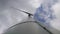 Closeup footage from below of a giant wind turbine with three blades with the sky and clouds in the background producing clean ene