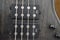 Closeup of four bass strings and black pickups on a grey swamp ash bass body