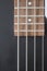 Closeup of four bass strings and black pickups on a grey swamp ash bass body