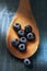 Closeup of fresh blueberries on a wooden spoon laying on a rustic painted farmhouse style kitchen table with warm side light