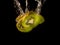 Closeup of fresh kiwis slices falling into clear water with big splash on black background. Group of juicy kiwi falling into water