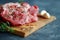 Closeup of fresh pork steaks, chops sprinkled with spices and rosemary on a wooden cutting board and a row of garlic cloves. Dark