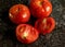 Closeup of fresh ripe tomatoes with water droplets on a black granite kitchen counter surface