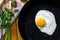 Closeup of fried egg in a black cast-iron pan without oil, sprinkled with salt strag with fresh parsley and garlic. Concept