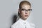 Closeup frontal portrait of a blonde woman with makeup wearing eyeglasses, looking at camera, over grey background.