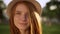 Closeup gentle attractive lady in hat with nice red long hair looking at camera touching hair smiling during bright