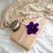 Closeup of a gift wrapped in brown paper with a violet flower and a wooden spool with white ribbon