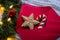 Closeup gingerbread in form of star and caramel cane in red envelope near festive decoration with Christmas balls and warm garland