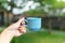 Closeup, girl holds in her hand a blue cup with a drink on a blurred background of a green yard