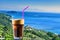 Closeup of a glass of iced coffee on background of a beautiful view of the Aegean sea