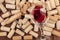 A closeup of a glass of red wine with a corkscrew on top of many wine corks