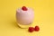 Closeup of a glass of sweet yogurt with a fresh raspberry on top on a yellow background