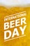 Closeup of a glass of yellow foamy craft beer with international Beer day text