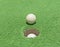 Closeup of golf ball by hole on green astroturf