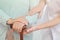 Closeup of grandmother`s hands on wooden cane, helpful granddaughter