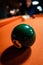 Closeup of a green ball on an orange billiard board under the light