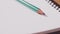 Closeup of a green pencil on a notebook. Notepad open on a blank page on the table