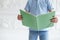 Closeup of green textbook in hands of young boy in blue t-shirt