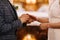 Closeup of a groom putting on the golden ring on the bride& x27;s finger with a blurry background