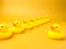 Closeup of a group of rubber ducks with a leader isolated on yellow background- teamwork concept