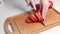 Closeup of hand of female cutting fresh tomato using kitchen knife on wooden cutting board