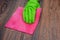 Closeup of a hand in a green rubber glove rubbing a wet wooden surface.