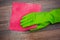 Closeup of a hand in a green rubber glove rubbing a wet wooden surface.