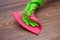 Closeup of a hand in a green rubber glove rubbing a wet wooden surface.