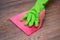 Closeup of a hand in a green rubber glove rubbing a wet wooden surface.