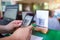 Closeup of a hand holding phone and scanning QR code with blurry cashier at counter service. Man hands paying with QR code.