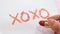 Closeup of hand holding a tube of red lipstick, with the symbol `XOXO` written