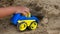 Closeup hand of little child boy playing car toy on sand outdoor in rural nature background.