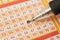 Closeup of hand marking number on lottery ticket with pen.